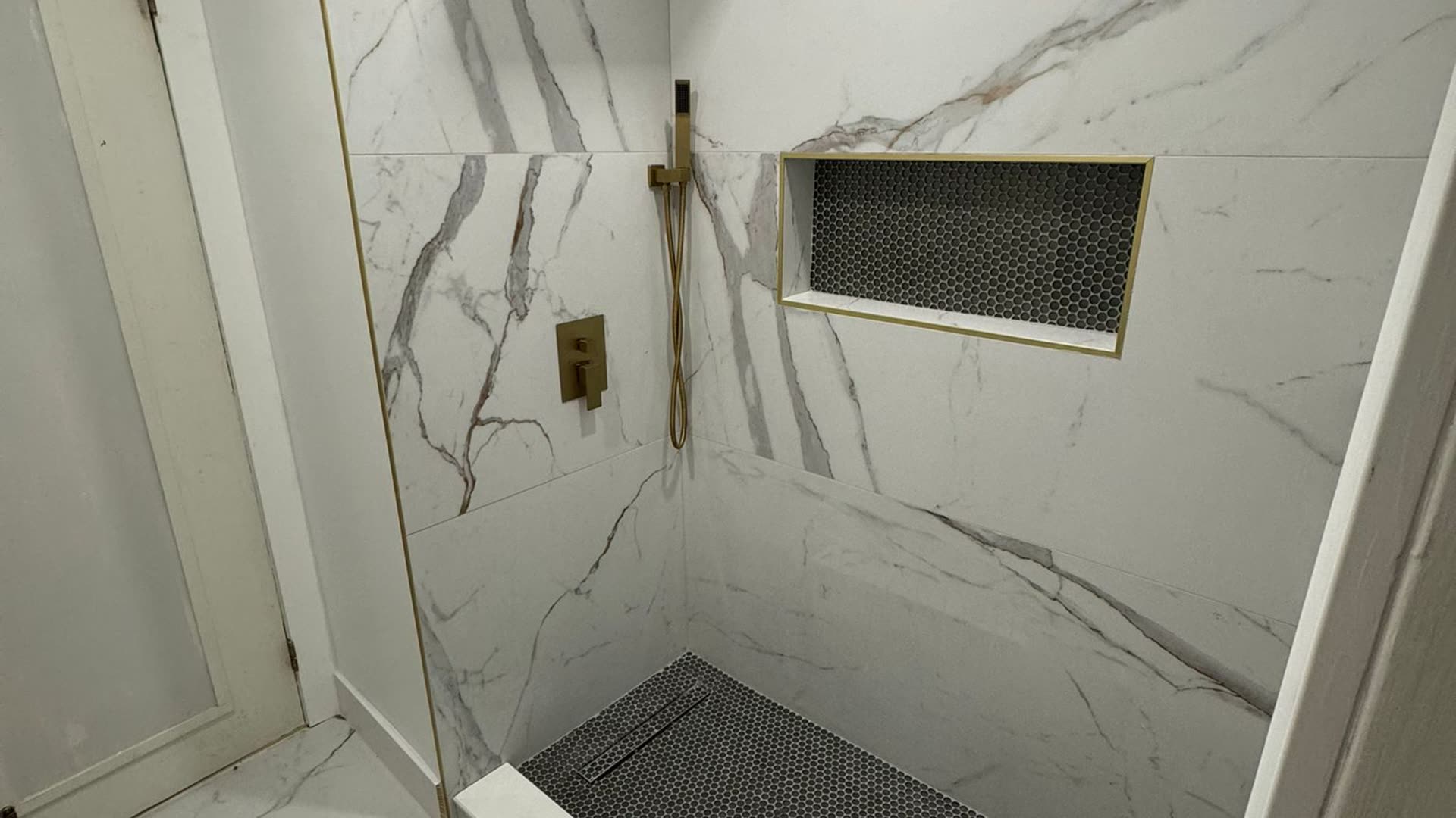 Walk-in shower finished in large-format marble-look porcelain, with a recessed niche, a linear drain at the back wall and a fixed glass panel