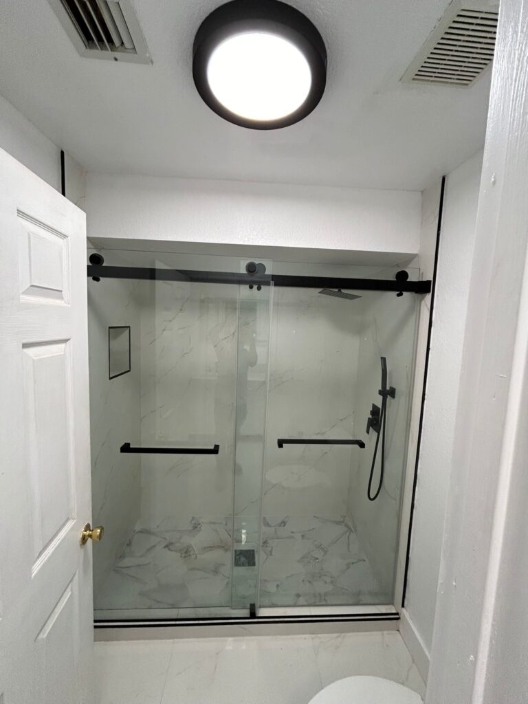 Walk-in shower enclosed with sliding glass panels on a black track, with a grab rail fixed to the tiled wall
