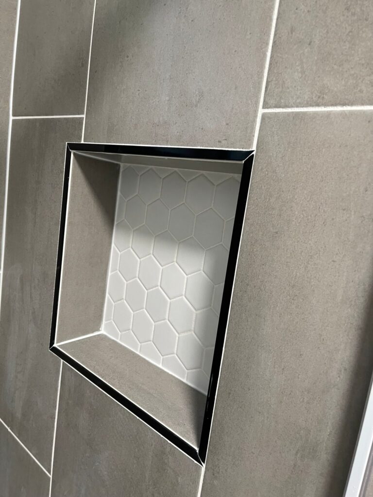 Recessed shower niche framed with a dark trim and lined with hexagonal mosaic tile