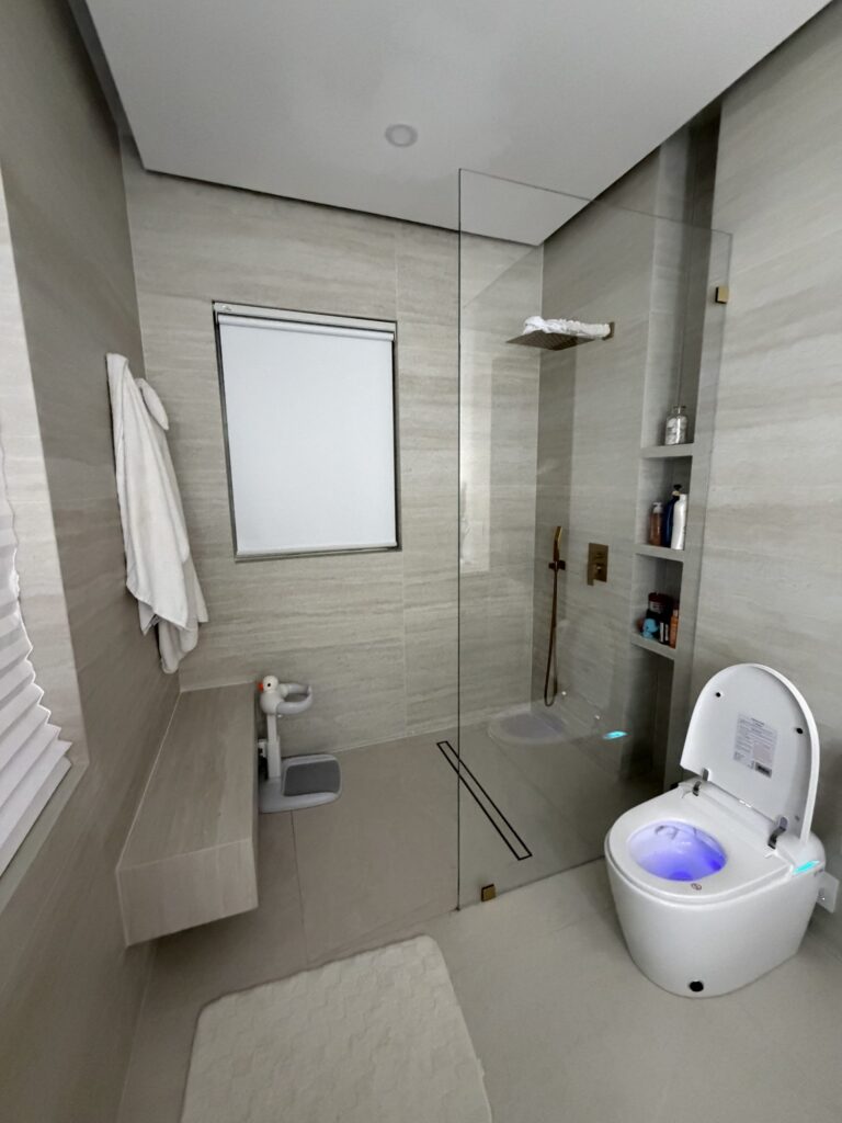 Walk-in shower with a glass screen alongside a wall-hung toilet, finished in pale large-format tile