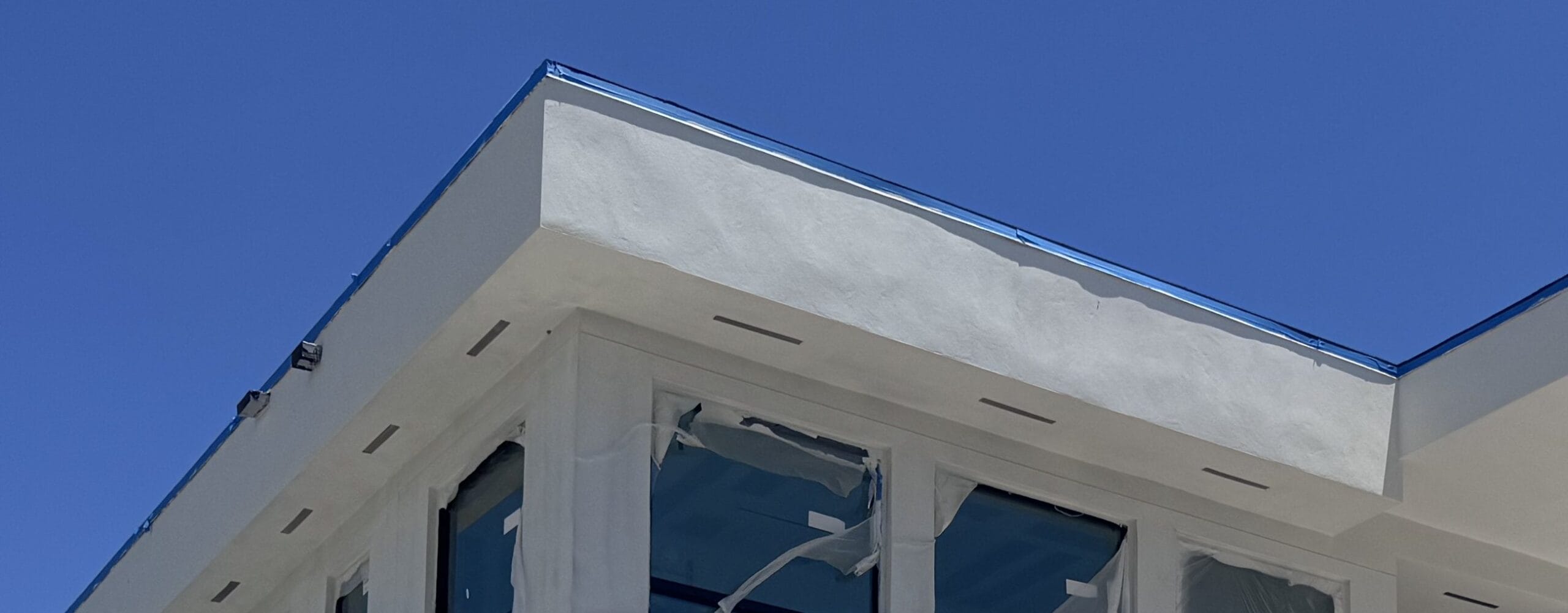 Close-up of the parapet roof edge showing the stucco return and the metal drip flashing