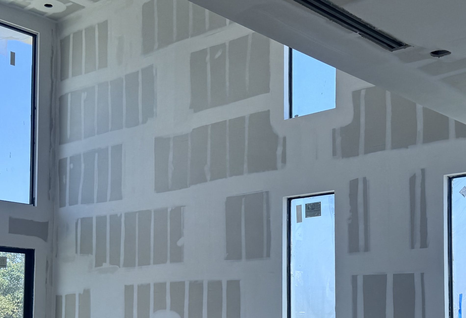 Close-up of taped and floated drywall joints against a two-storey window opening