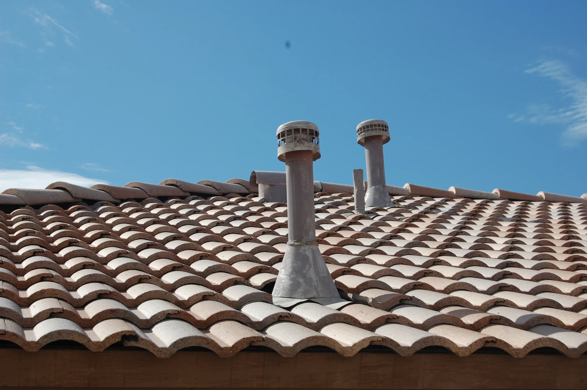 Barrel tile roof with vent stacks against a clear sky