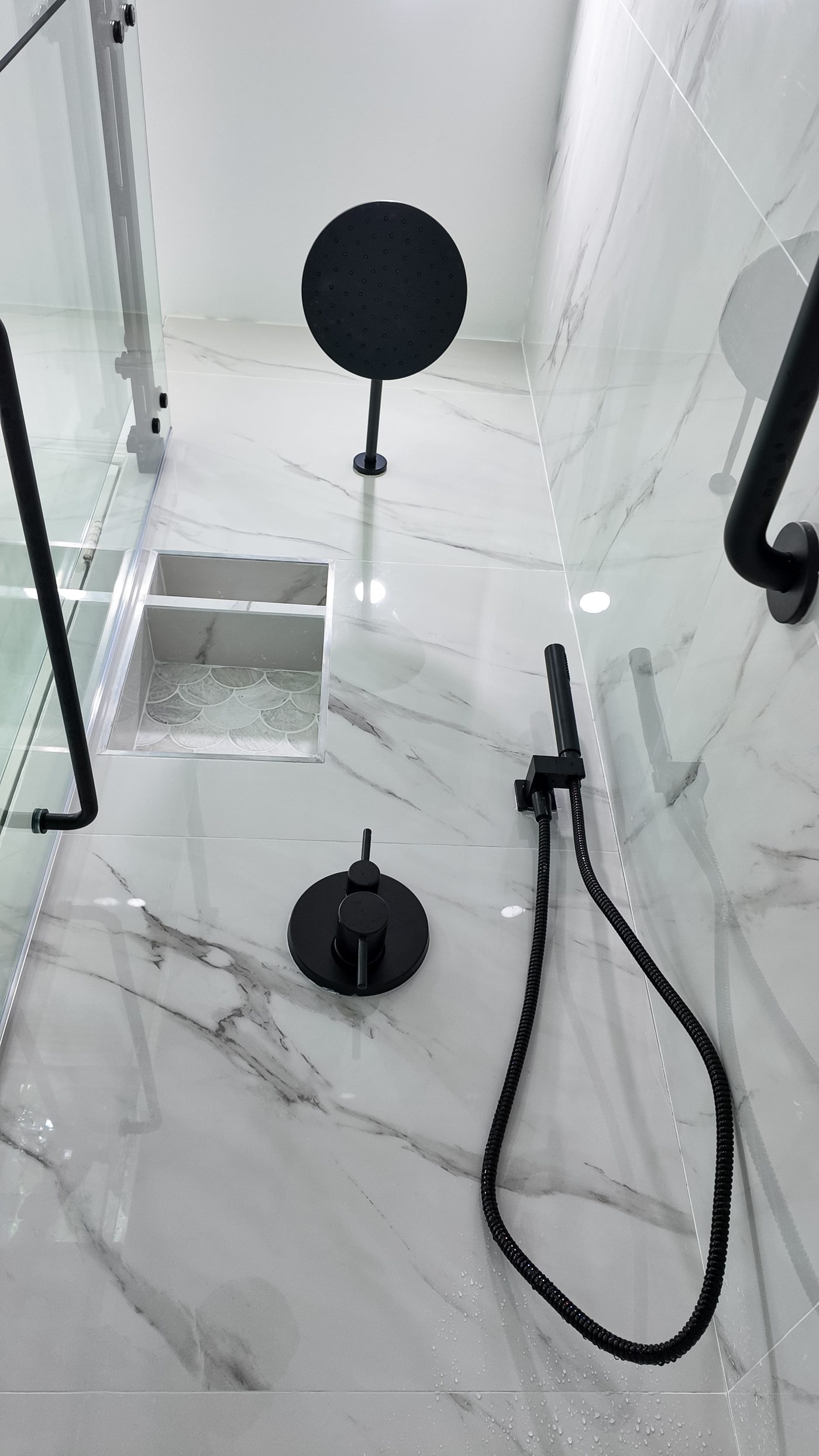 Walk-in shower lined in marble-look porcelain with a matt black rain head and hand shower