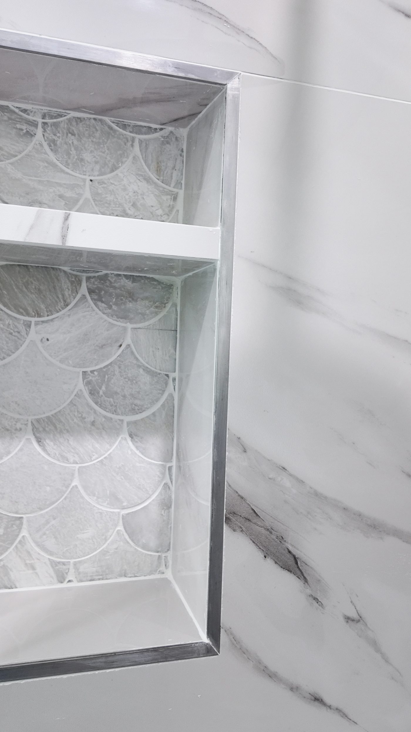 Recessed shower niche with a scalloped mosaic back and a stone shelf