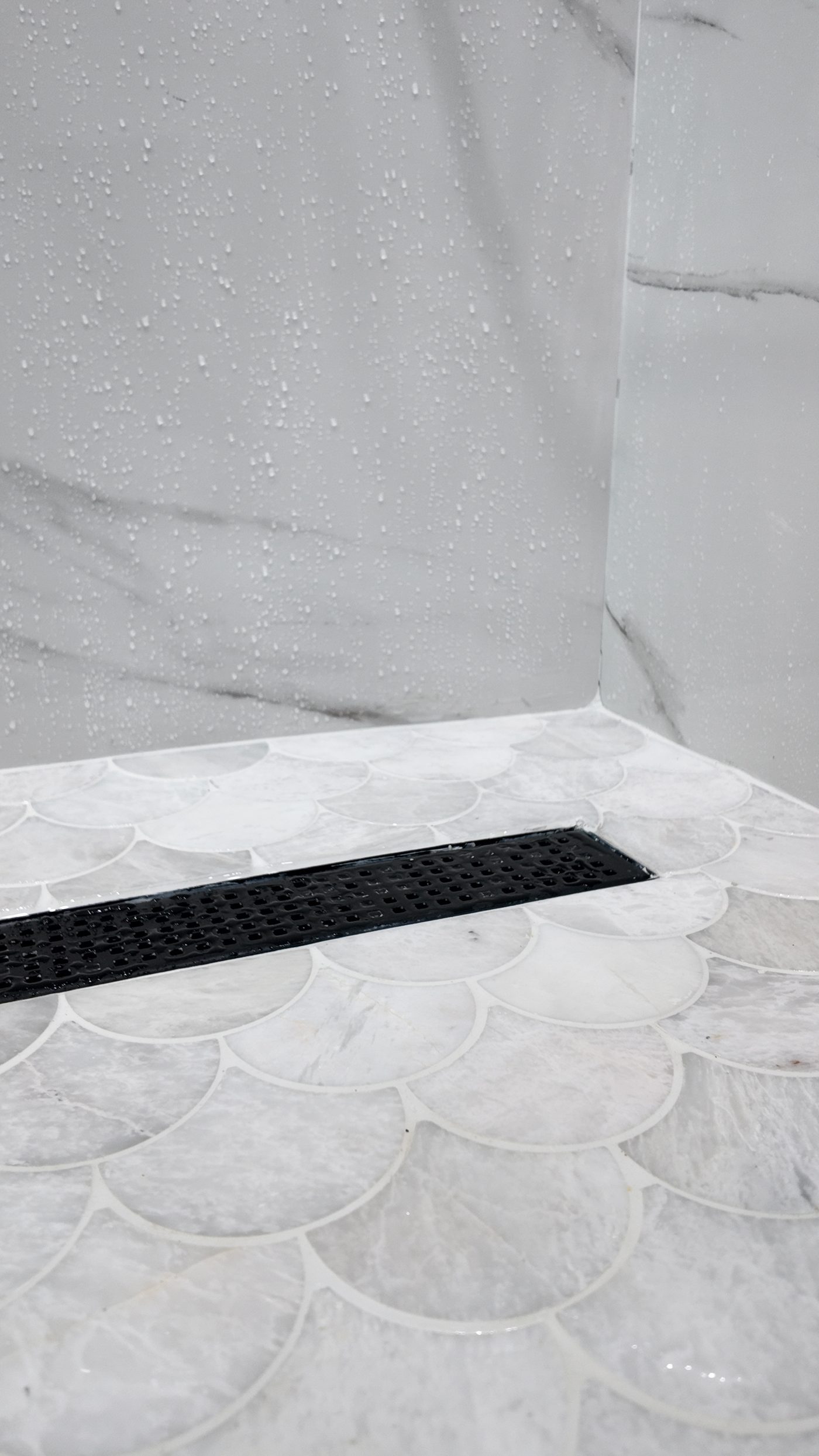 Scalloped mosaic shower floor with a matt black linear drain set into the fall