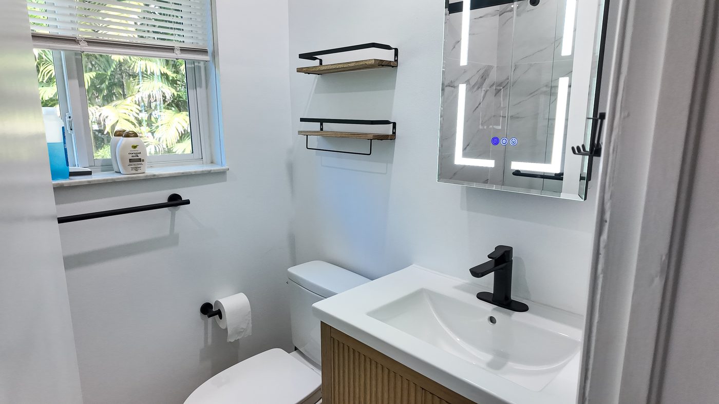 Bathroom with a fluted vanity, backlit mirror cabinet, towel rail and window