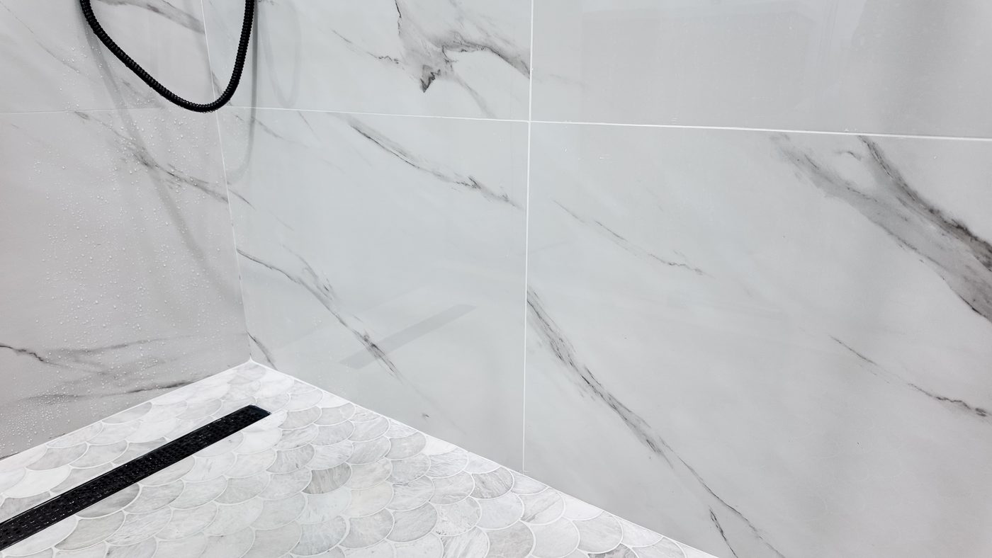 Large-format marble-look wall tile meeting the mosaic floor at the shower threshold
