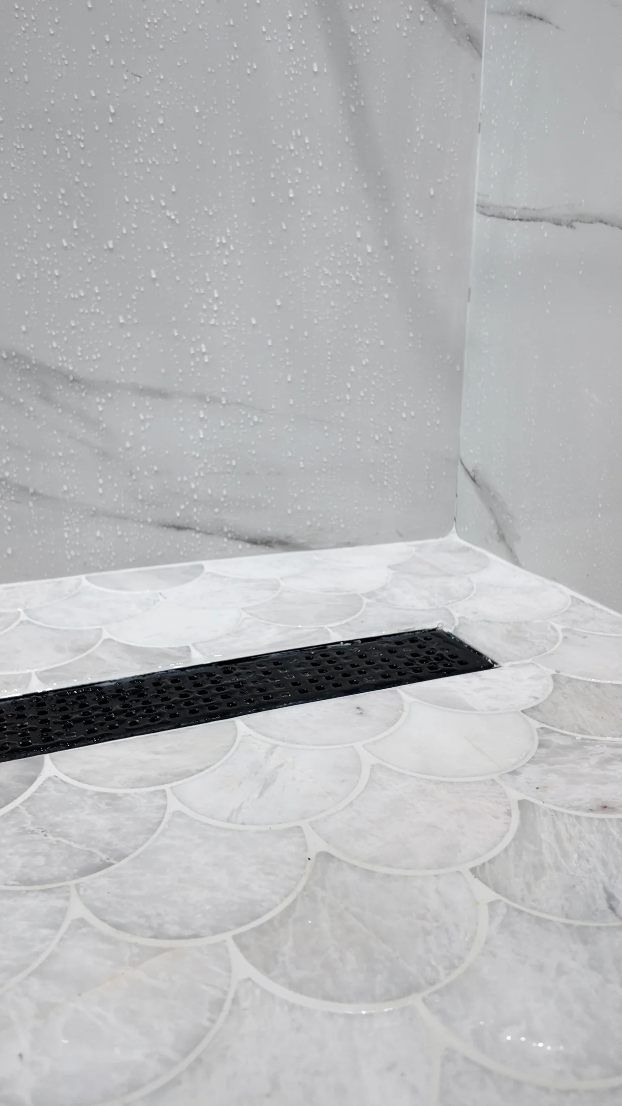 Shower floor laid in fan-pattern mosaic tile falling to a linear drain
