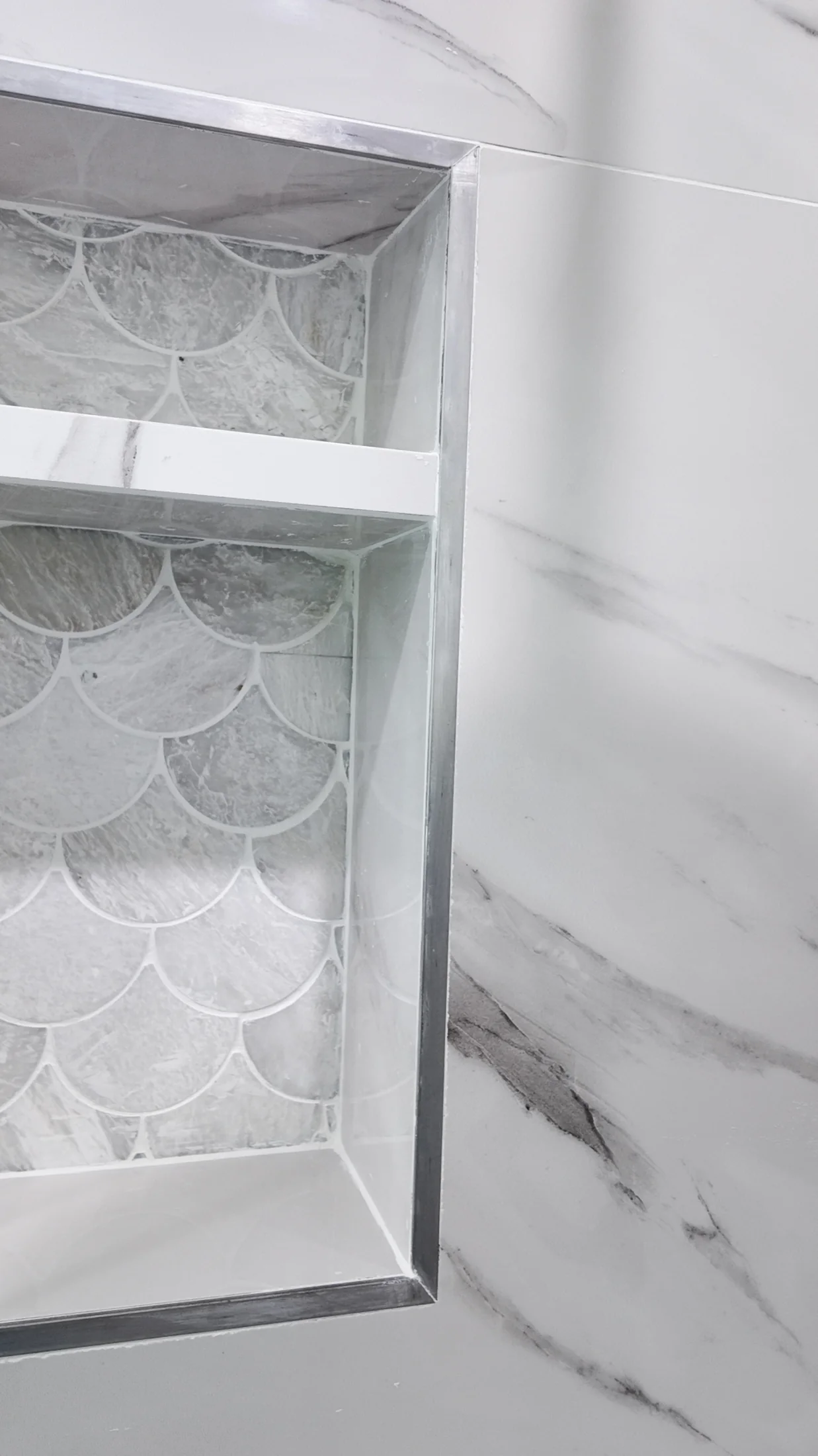 Recessed shower niche lined with fan-pattern mosaic tile and a metal trim edge