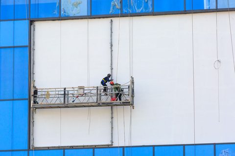 Two workers on exterior scaffolding renovating a commercial building facade