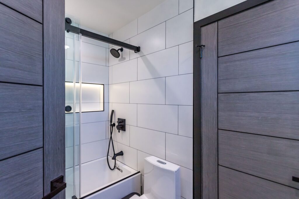 Bathroom remodel by Elbaz Construction in South Florida: large-format white wall tile, matt black brassware, a blue shaker vanity with a marble top and a patterned floor