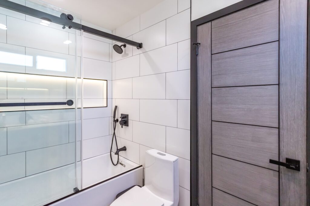 Bathroom remodel by Elbaz Construction in South Florida: large-format white wall tile, matt black brassware, a blue shaker vanity with a marble top and a patterned floor