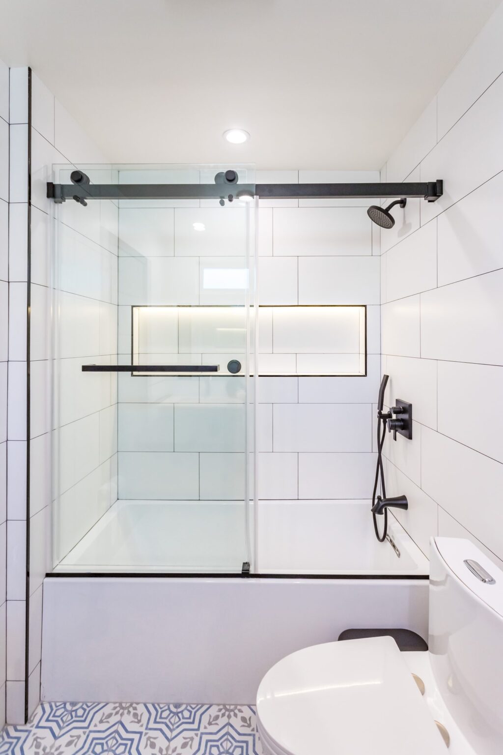Bathroom remodel by Elbaz Construction in South Florida: large-format white wall tile, matt black brassware, a blue shaker vanity with a marble top and a patterned floor