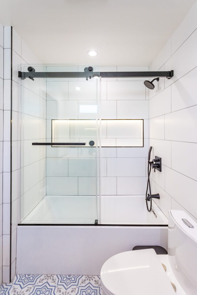 Bathroom remodel by Elbaz Construction in South Florida: large-format white wall tile, matt black brassware, a blue shaker vanity with a marble top and a patterned floor