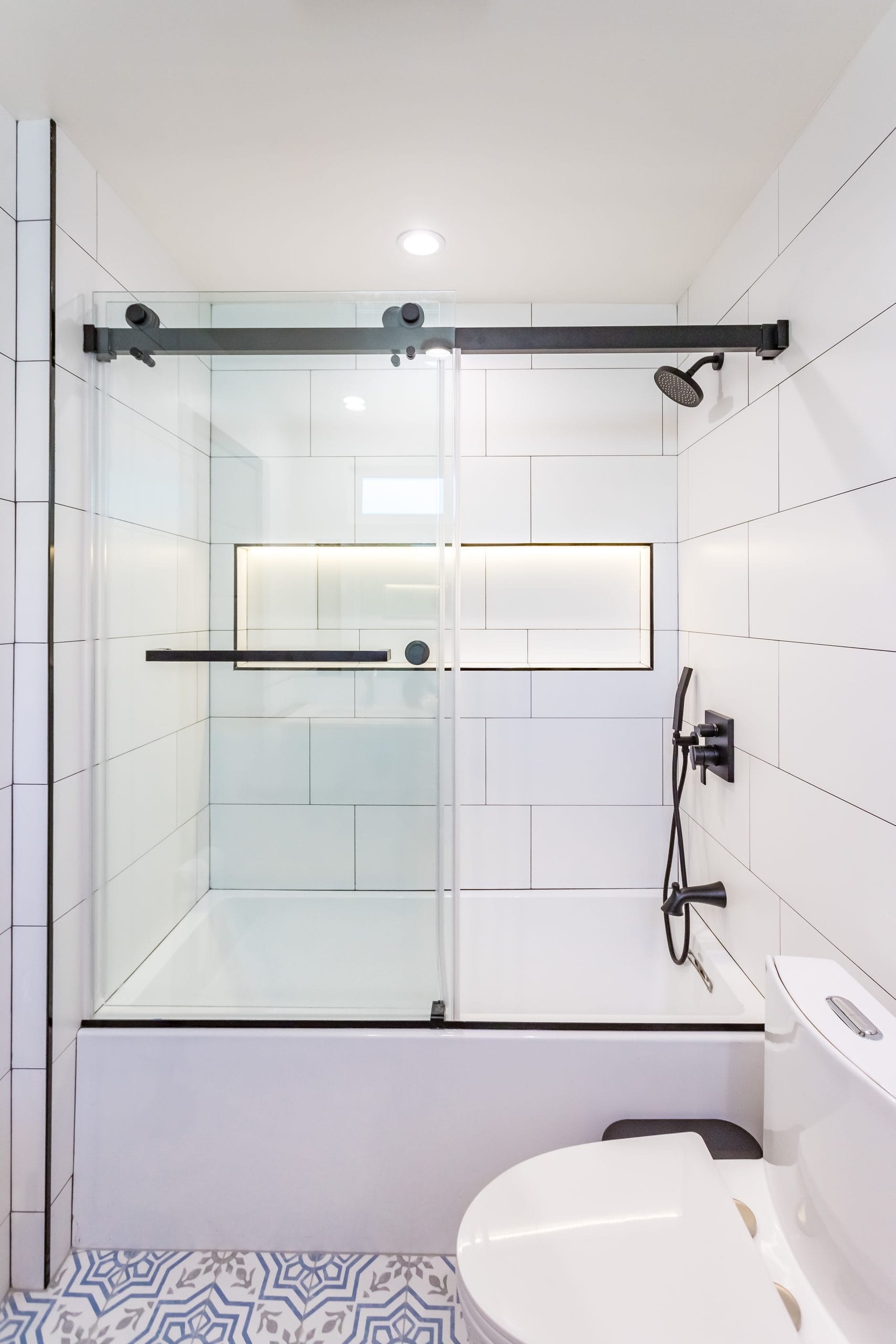 Bathroom remodel by Elbaz Construction in South Florida: large-format white wall tile, matt black brassware, a blue shaker vanity with a marble top and a patterned floor