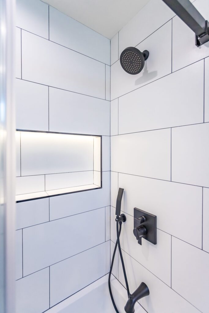 Bathroom remodel by Elbaz Construction in South Florida: large-format white wall tile, matt black brassware, a blue shaker vanity with a marble top and a patterned floor
