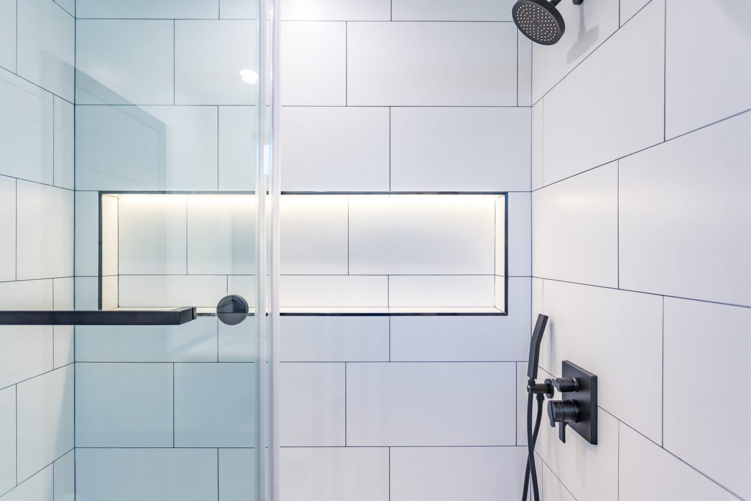 Bathroom remodel by Elbaz Construction in South Florida: large-format white wall tile, matt black brassware, a blue shaker vanity with a marble top and a patterned floor