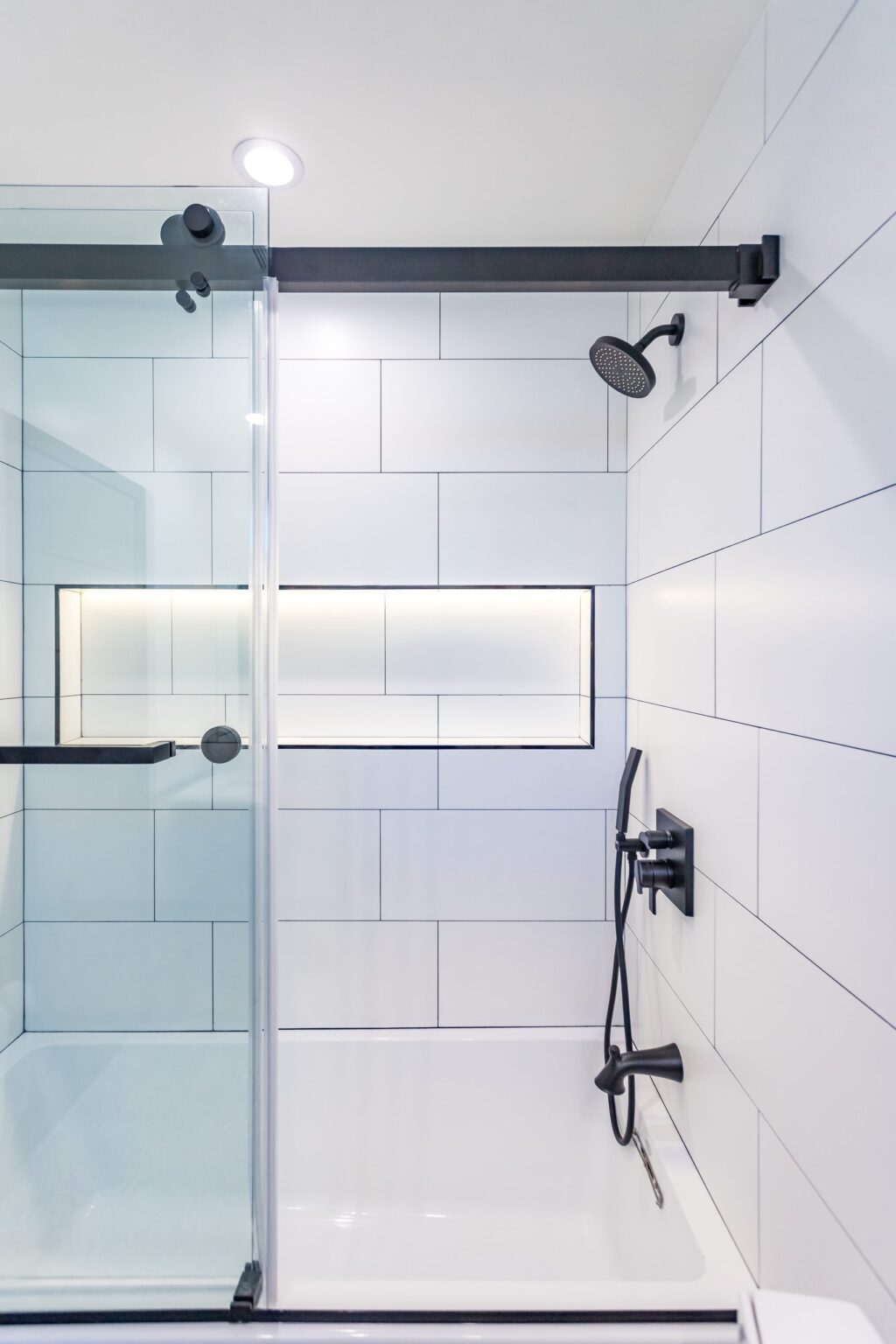 Bathroom remodel by Elbaz Construction in South Florida: large-format white wall tile, matt black brassware, a blue shaker vanity with a marble top and a patterned floor