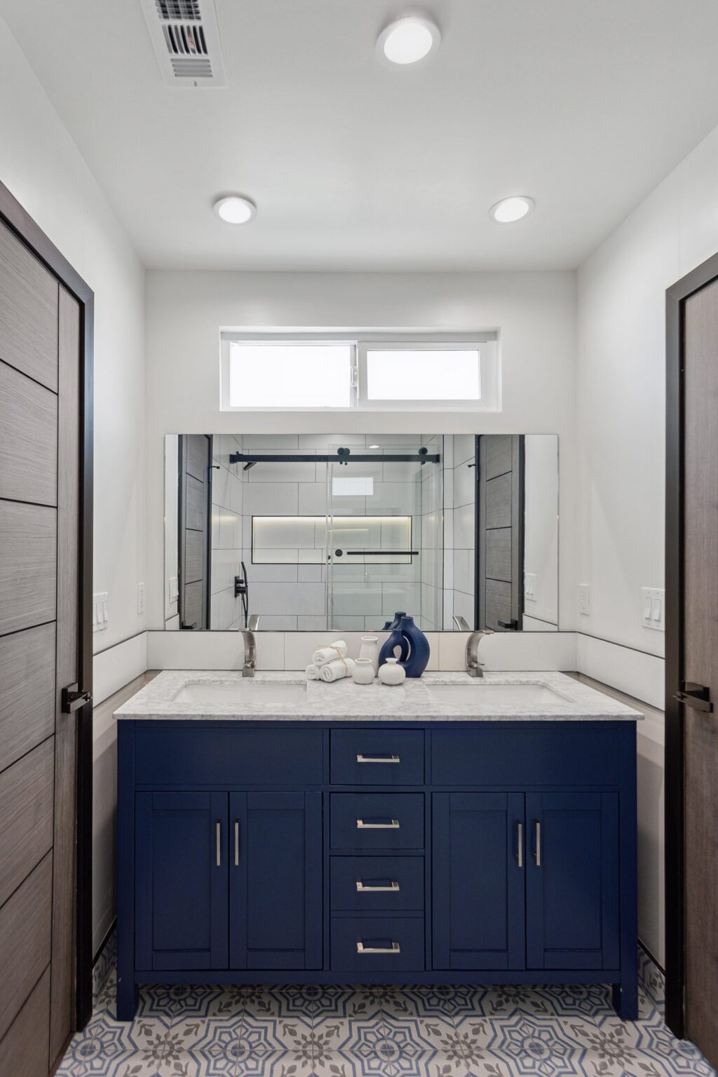 Bathroom remodel by Elbaz Construction in South Florida: large-format white wall tile, matt black brassware, a blue shaker vanity with a marble top and a patterned floor