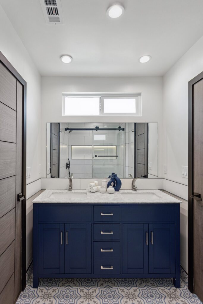 Bathroom remodel by Elbaz Construction in South Florida: large-format white wall tile, matt black brassware, a blue shaker vanity with a marble top and a patterned floor