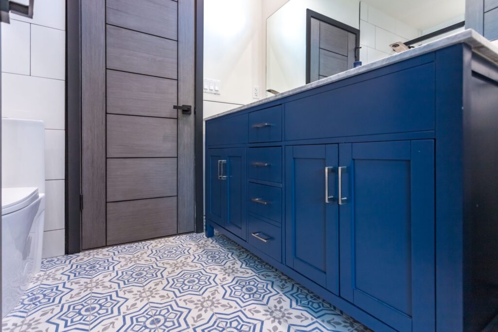 Navy shaker double vanity with a marble top and brushed handles, above a patterned blue and white tiled floor, by Elbaz Construction