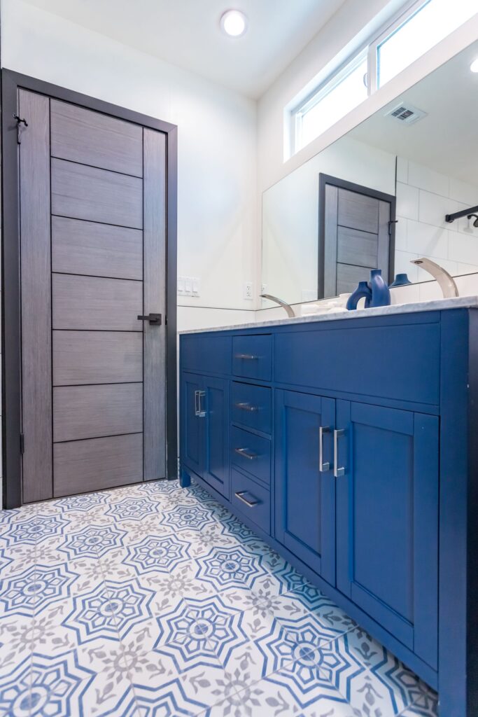 Bathroom remodel by Elbaz Construction in South Florida: large-format white wall tile, matt black brassware, a blue shaker vanity with a marble top and a patterned floor