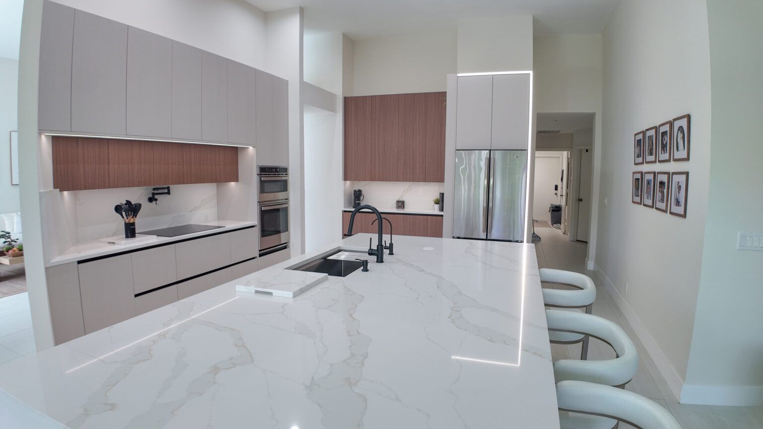 Open-plan kitchen and living remodel by Elbaz Construction in South Florida: handleless cabinetry, walnut wall units, large-format porcelain worktops and a screened terrace beyond the glazing