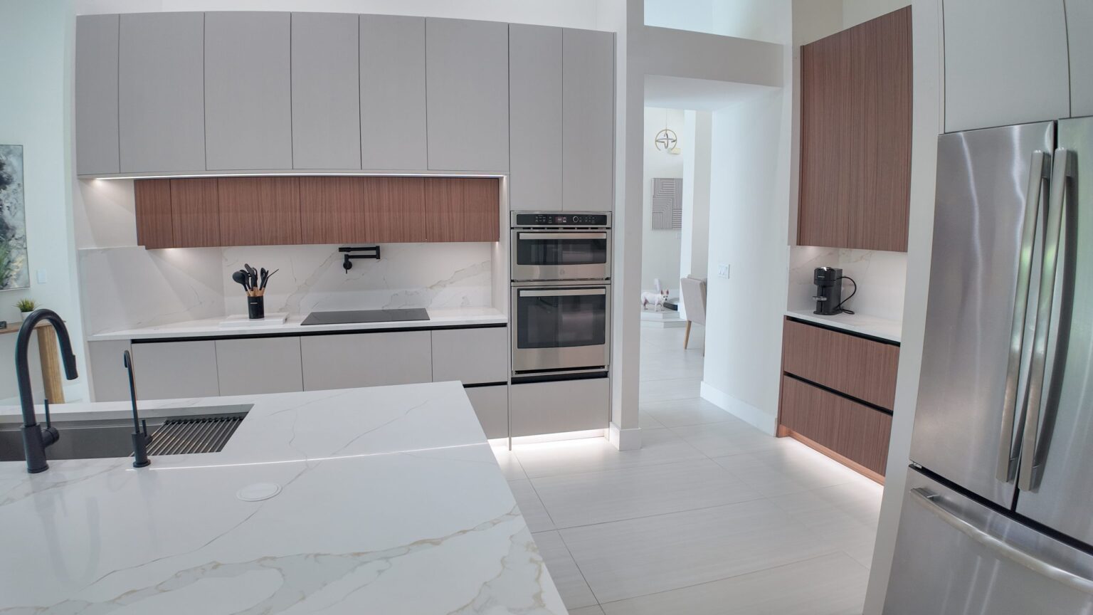 Open-plan kitchen and living remodel by Elbaz Construction in South Florida: handleless cabinetry, walnut wall units, large-format porcelain worktops and a screened terrace beyond the glazing
