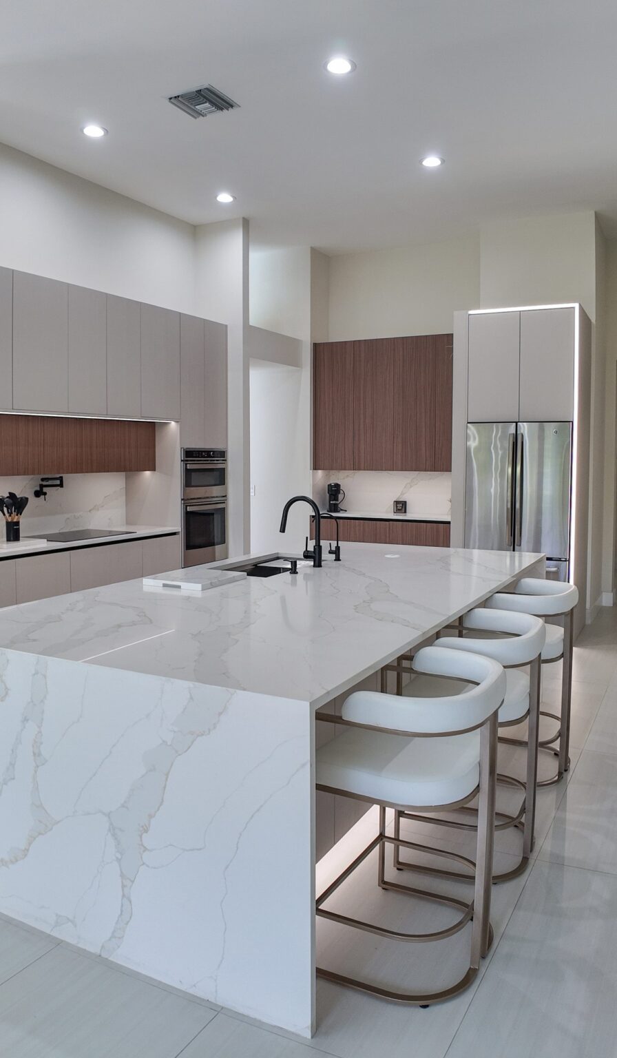 Open-plan kitchen and living remodel by Elbaz Construction in South Florida: handleless cabinetry, walnut wall units, large-format porcelain worktops and a screened terrace beyond the glazing