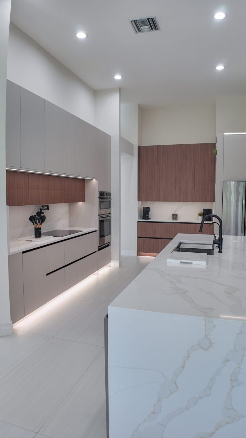 Open-plan kitchen and living remodel by Elbaz Construction in South Florida: handleless cabinetry, walnut wall units, large-format porcelain worktops and a screened terrace beyond the glazing