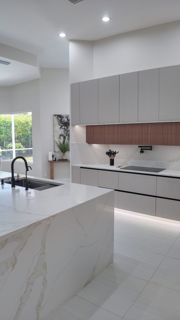 Open-plan kitchen and living remodel by Elbaz Construction in South Florida: handleless cabinetry, walnut wall units, large-format porcelain worktops and a screened terrace beyond the glazing