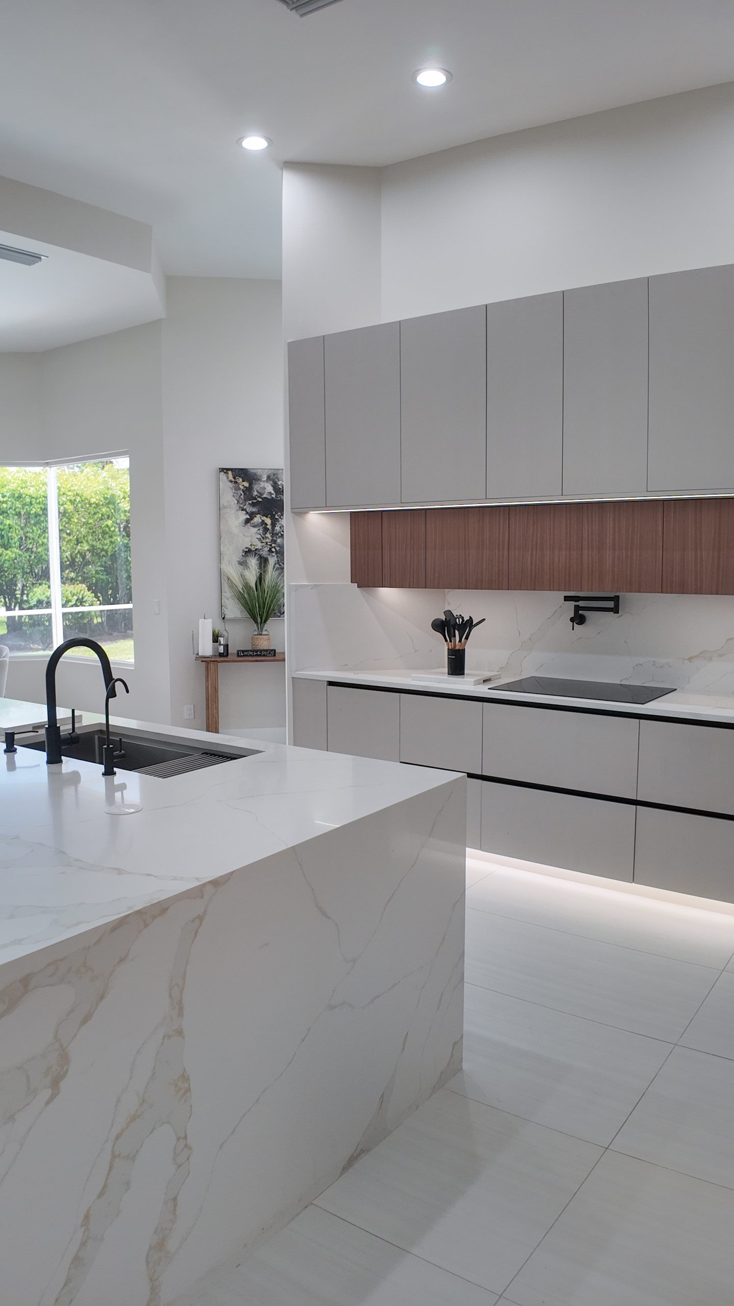 Kitchen island and sink run lit by daylight from the window wall behind