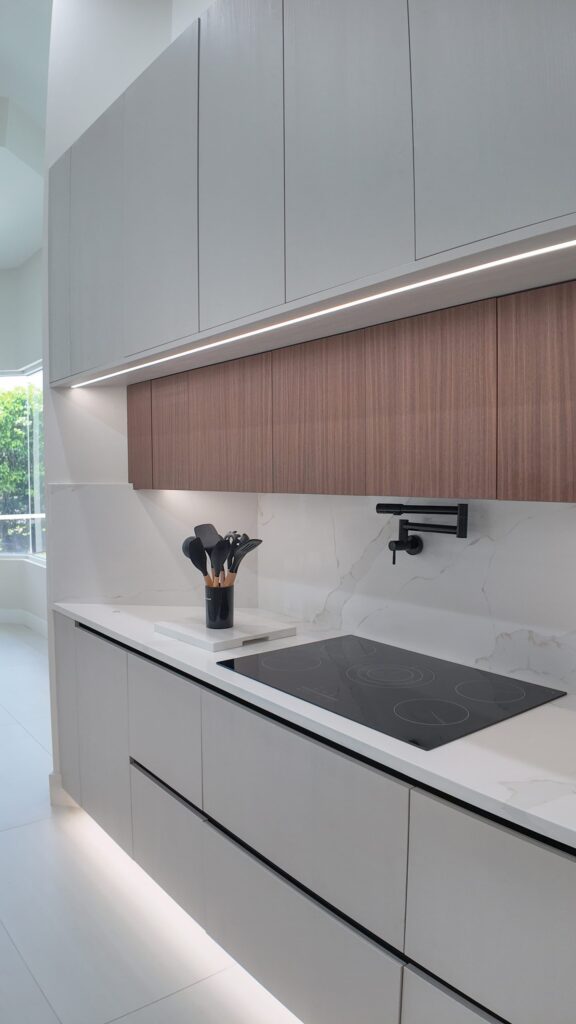 Open-plan kitchen and living remodel by Elbaz Construction in South Florida: handleless cabinetry, walnut wall units, large-format porcelain worktops and a screened terrace beyond the glazing