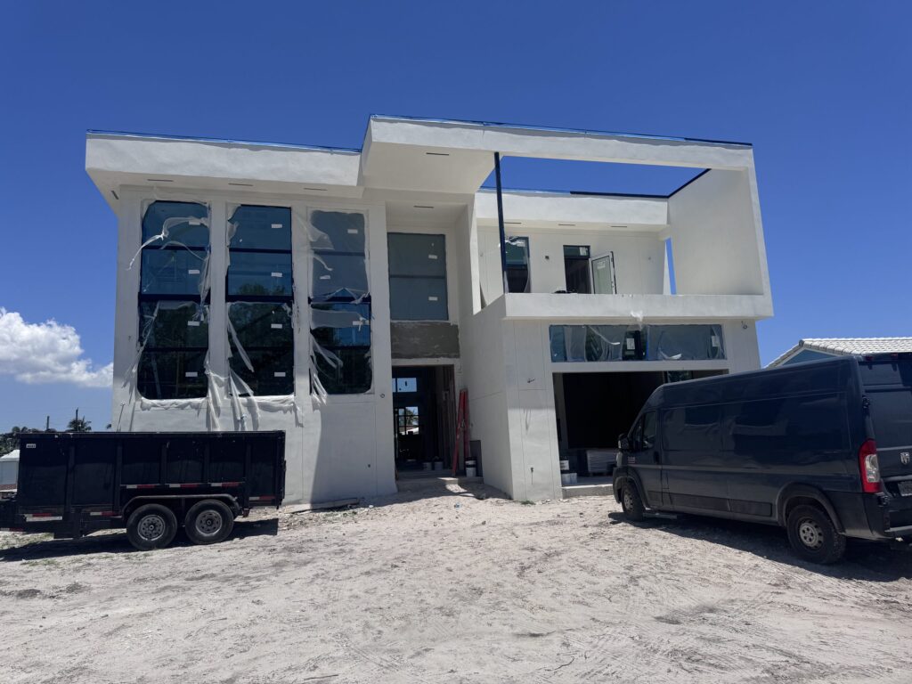 Custom home construction by Elbaz Construction on a South Florida canal lot: a two-storey house at the stucco and glazing stage, with the waterfront lot and dock behind it