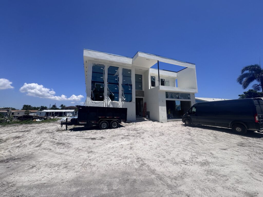 Custom home construction by Elbaz Construction on a South Florida canal lot: a two-storey house at the stucco and glazing stage, with the waterfront lot and dock behind it
