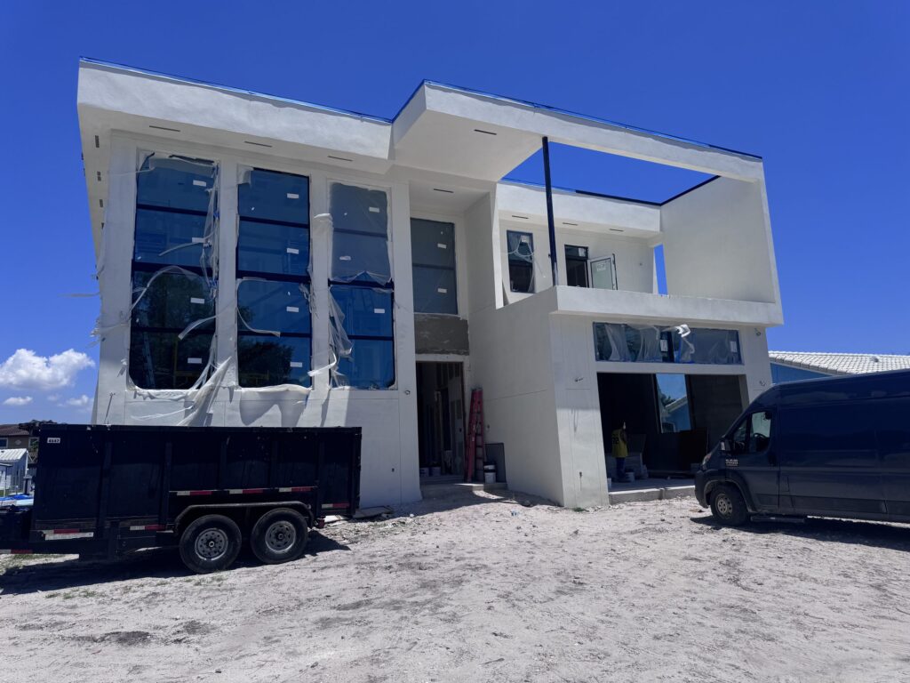 Custom home construction by Elbaz Construction on a South Florida canal lot: a two-storey house at the stucco and glazing stage, with the waterfront lot and dock behind it