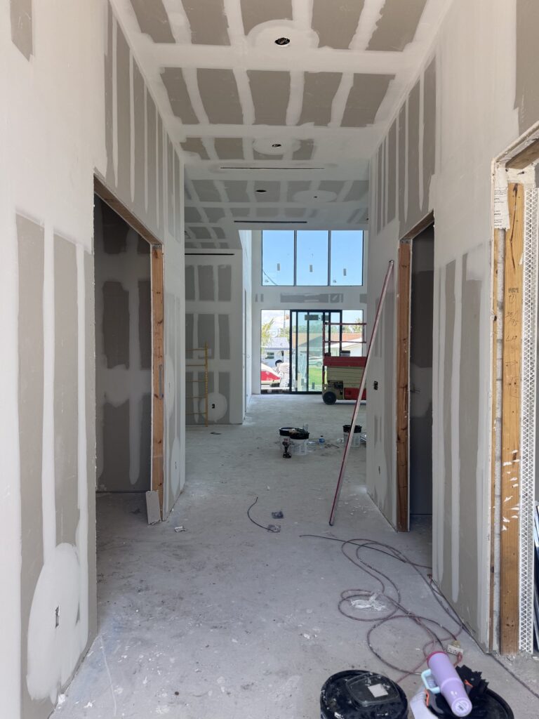 Interior of a custom home under construction by Elbaz Construction in South Florida: double-height glazing, a steel stair under installation and drywall at taping stage