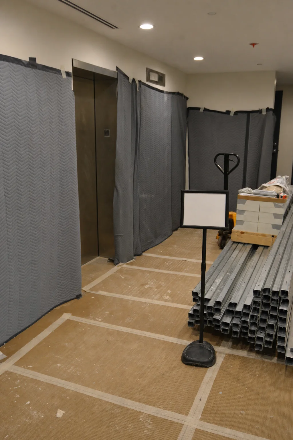 Illustration of freight elevator protection blankets, taped floor protection and staged metal studs and ceiling tiles in a building lobby during a fit-out