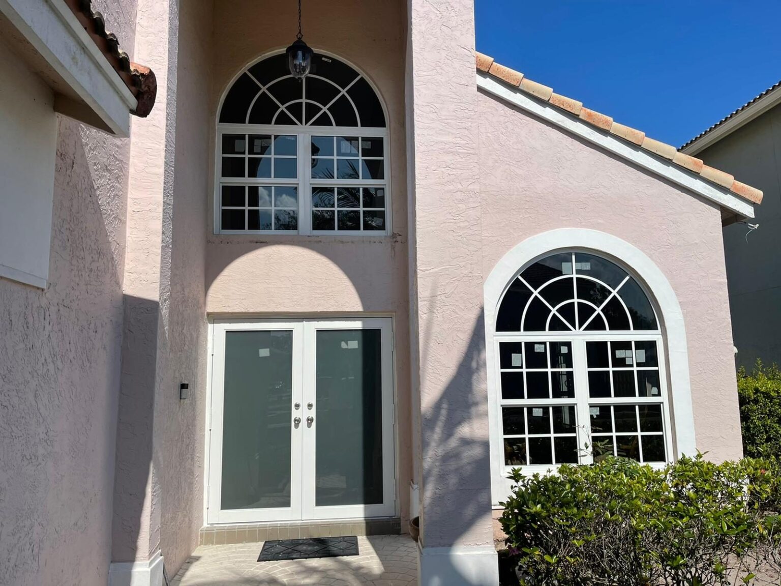 Front elevation of a stucco home with an arched transom over a pair of glazed entry doors and white-glazing-bar windows either side