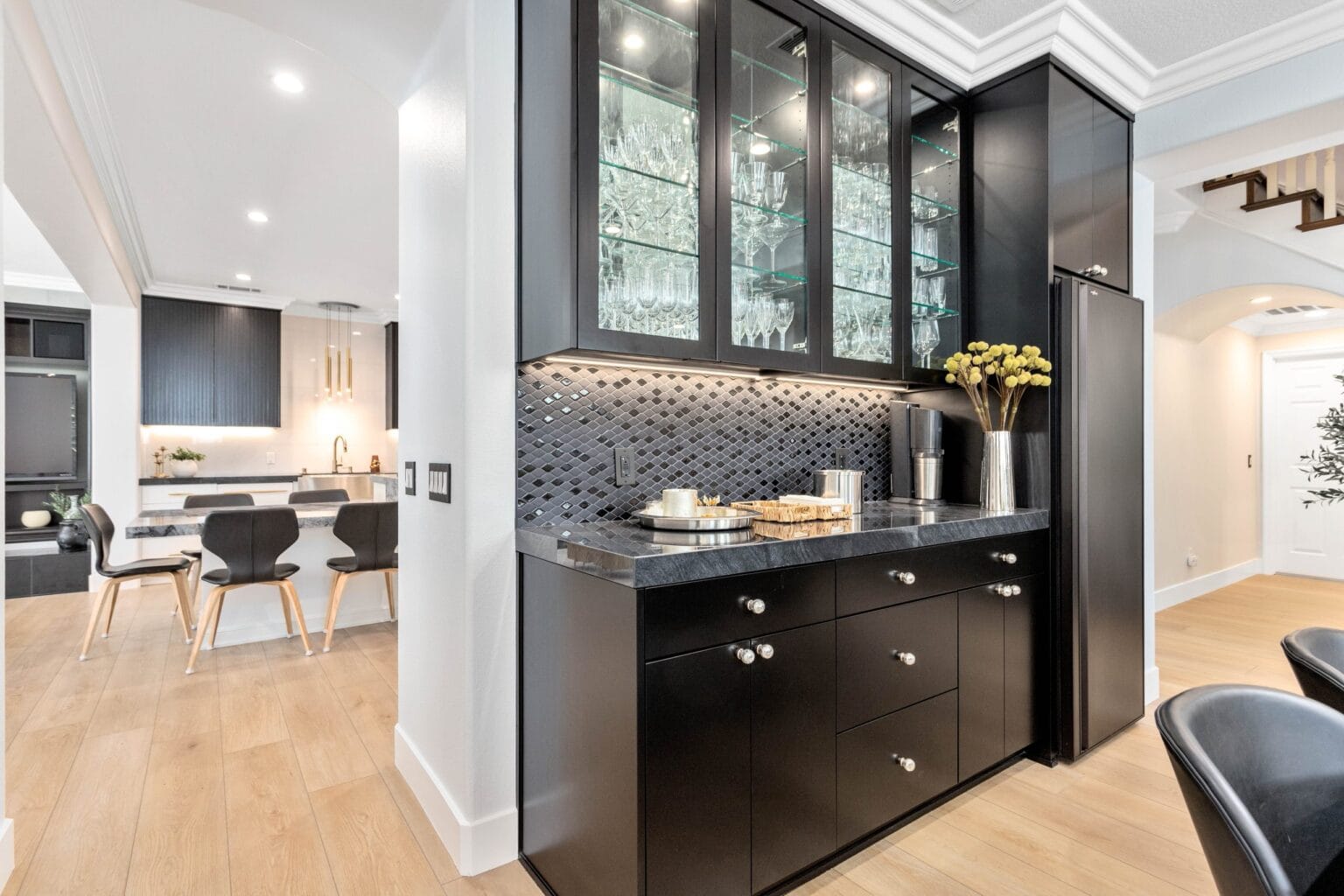 Black servery cabinetry with glass-fronted uppers, drawer bases and a mosaic splashback, opening through to the kitchen beyond