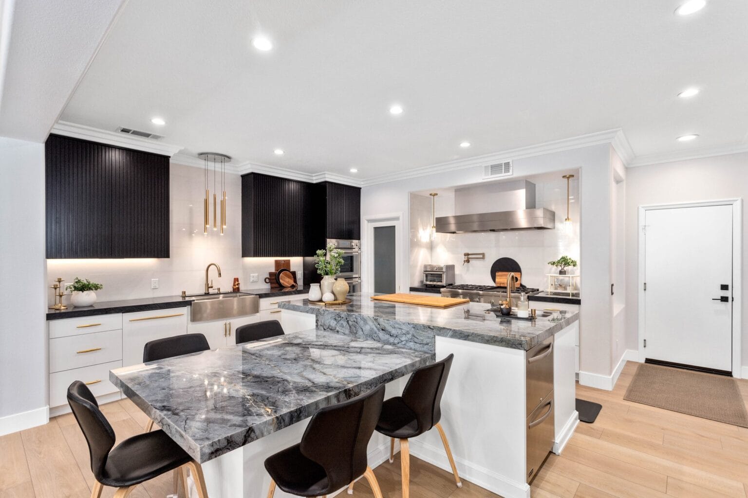 The kitchen seen from the dining end, with a grey-veined quartzite island, white cabinetry, a stainless hood and built-in wall ovens