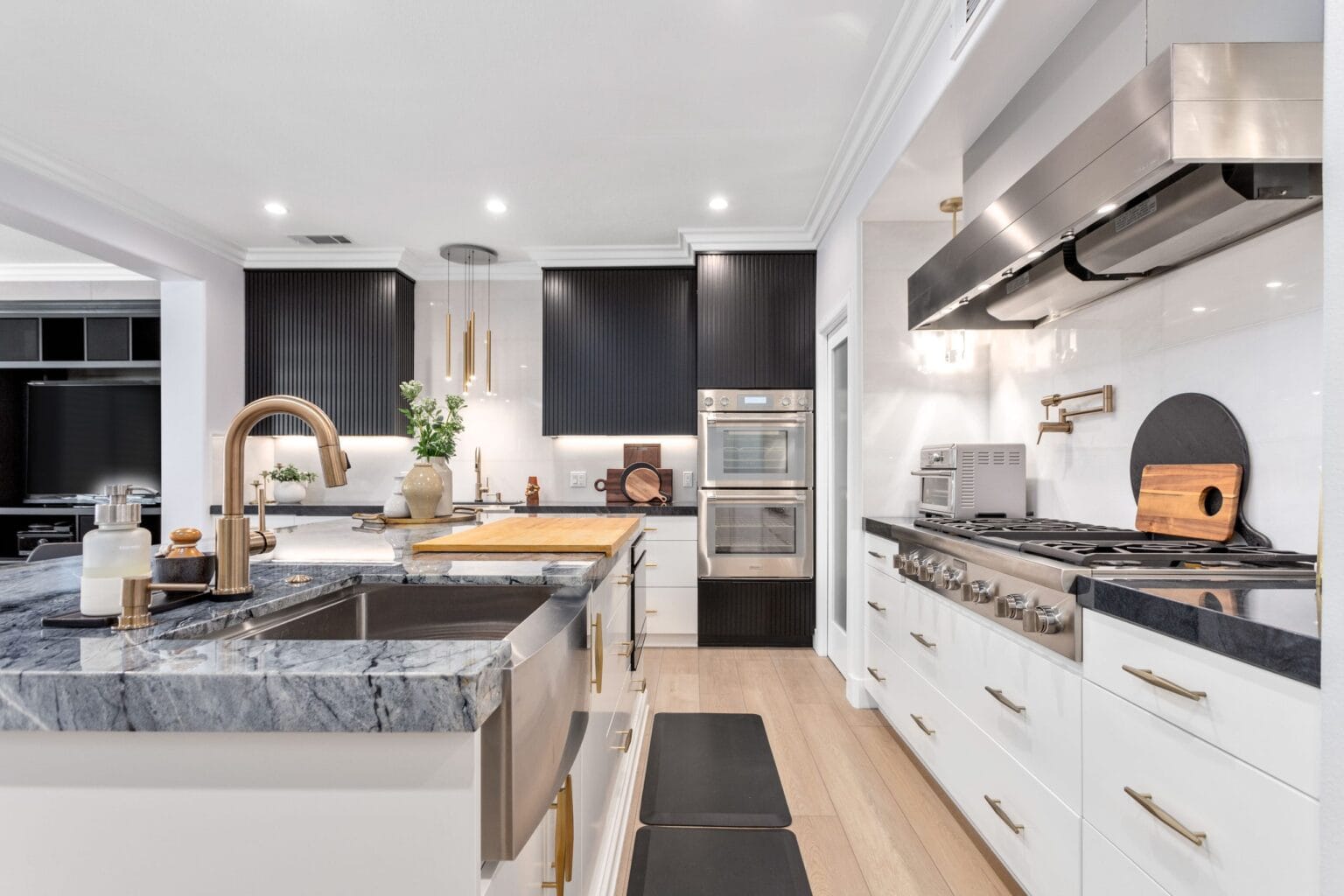 Quartzite island with an integrated sink and a brass gooseneck tap, black stone perimeter worktop, stainless range and wall ovens beyond