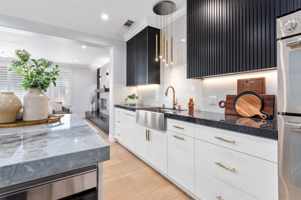 Island sink run in veined quartzite with black fluted tall units and a dark worktop beyond, on an Elbaz Construction interior remodel