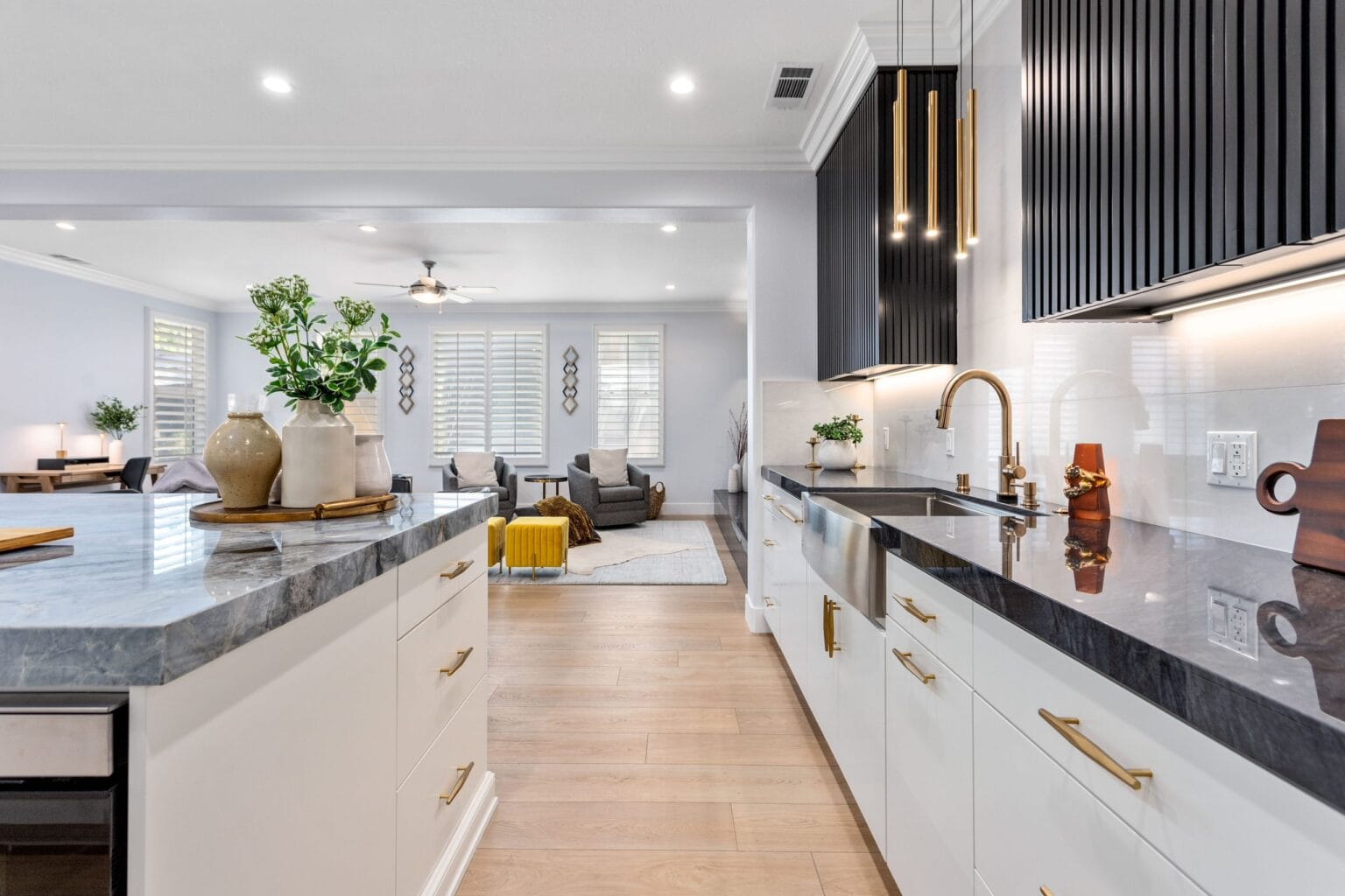 Stainless apron-front sink in a black stone worktop with a brass gooseneck tap, a white gloss splashback and a black fluted extractor above