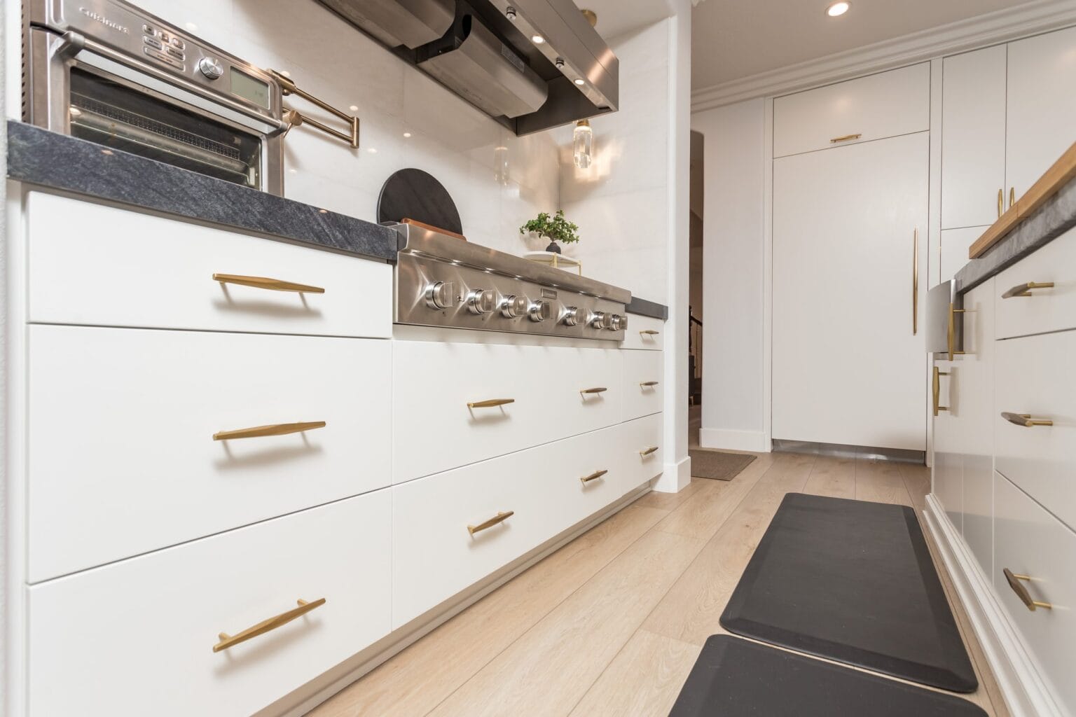 White base drawer run with brass bar handles below a dark stone worktop, on a pale timber floor