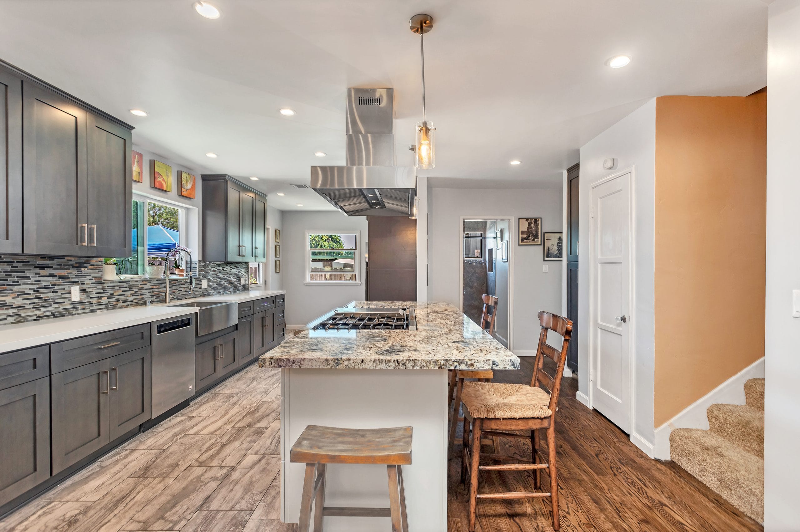 Remodelled kitchen with a granite-topped island, gas cooktop and stainless island hood, open to the hallway and stair