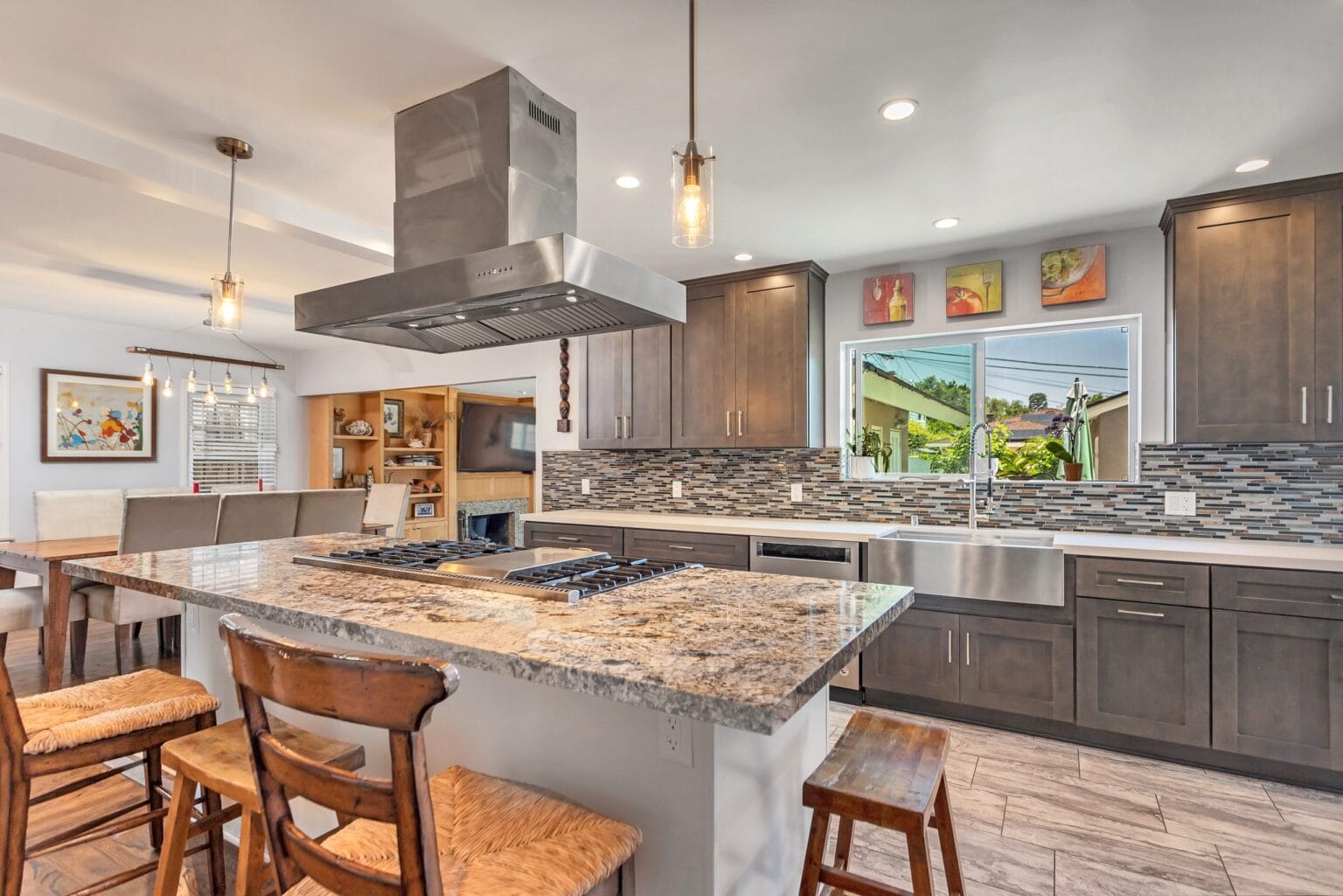 Open-plan kitchen by Elbaz Construction with a granite-topped island, a stainless island extractor, grey shaker cabinetry and a dining area beyond