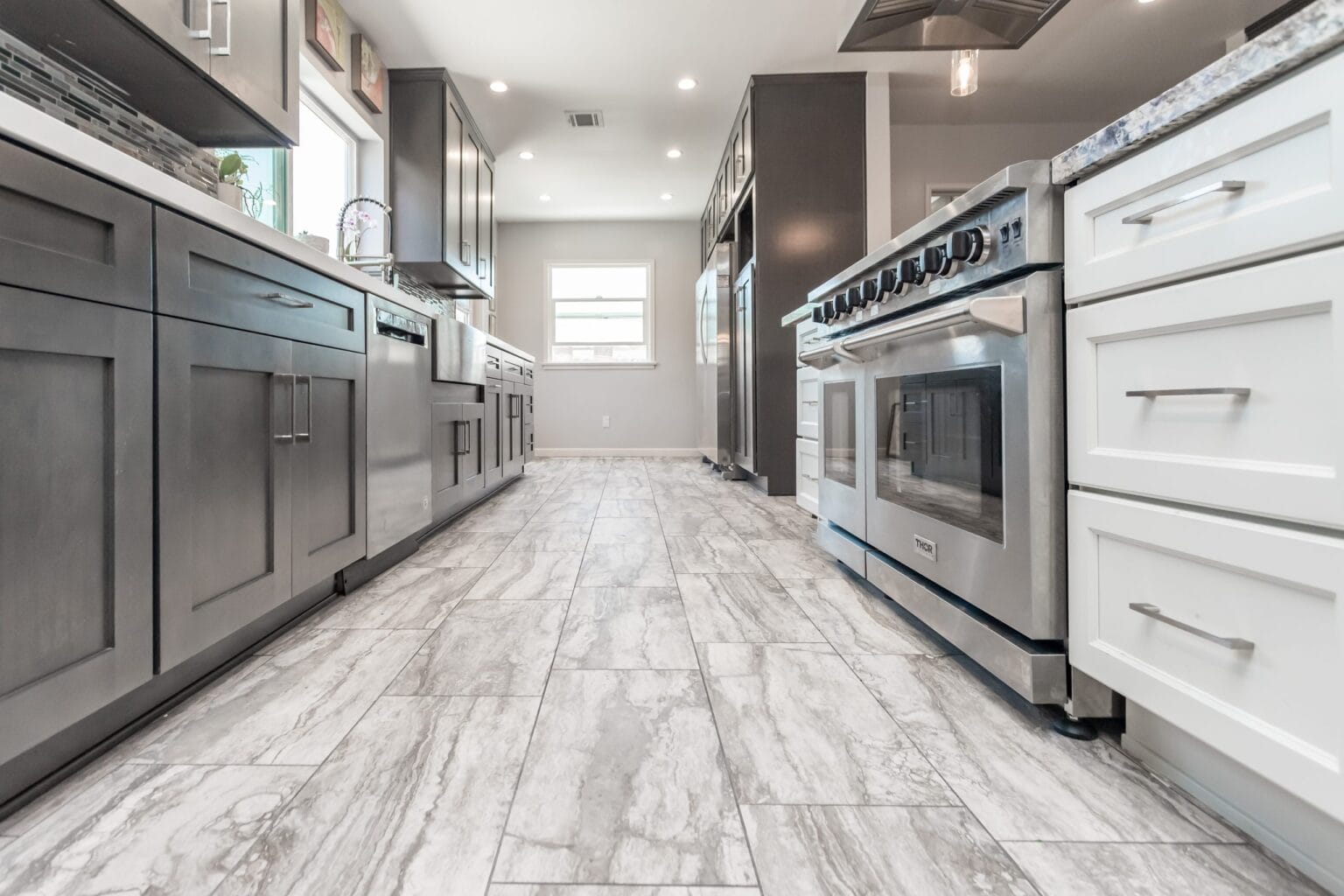 Perimeter cabinetry run with a stainless range and wall units, on a pale marble-look tiled floor