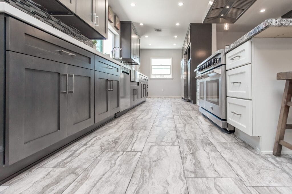The kitchen read down its length before styling, grey shaker units and a built-in oven tower over a large-format stone floor